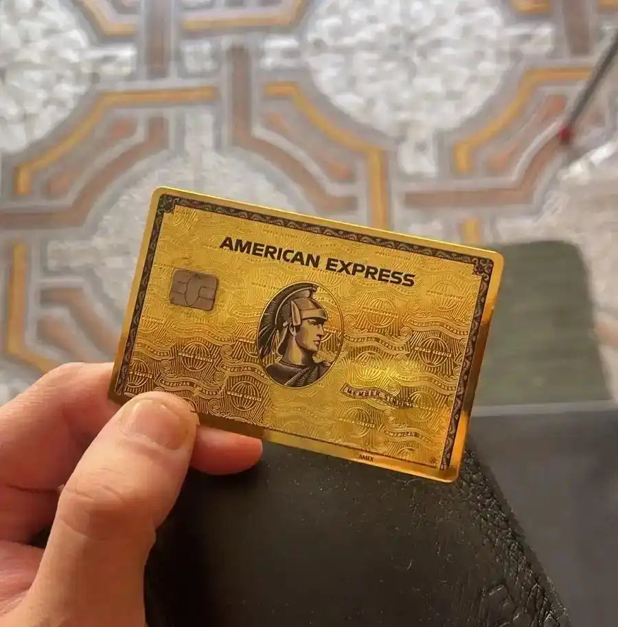 Hand holding a gold metal American Express card with detailed design and chip visible