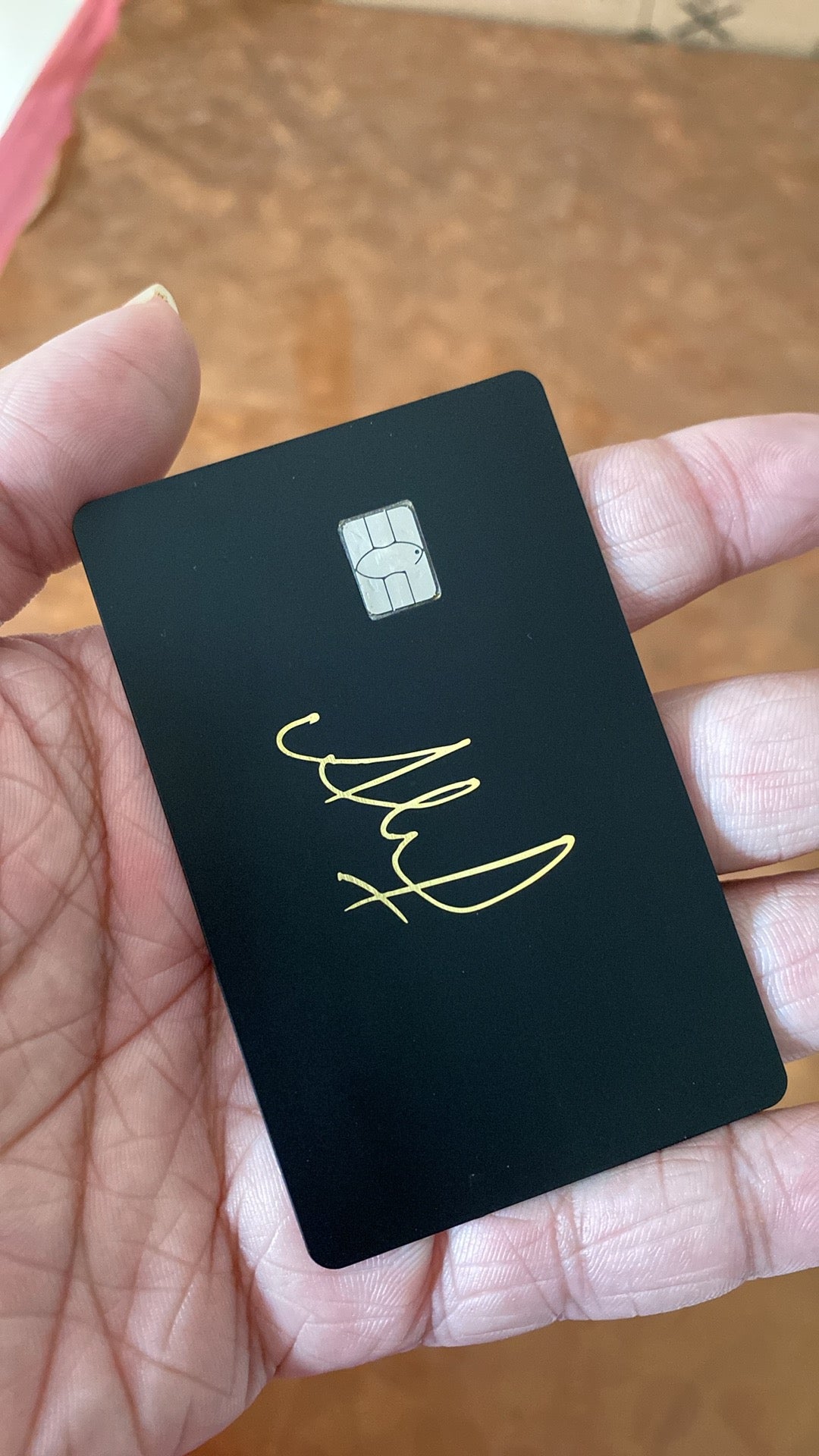Black metal card with gold signature and chip, held in a hand