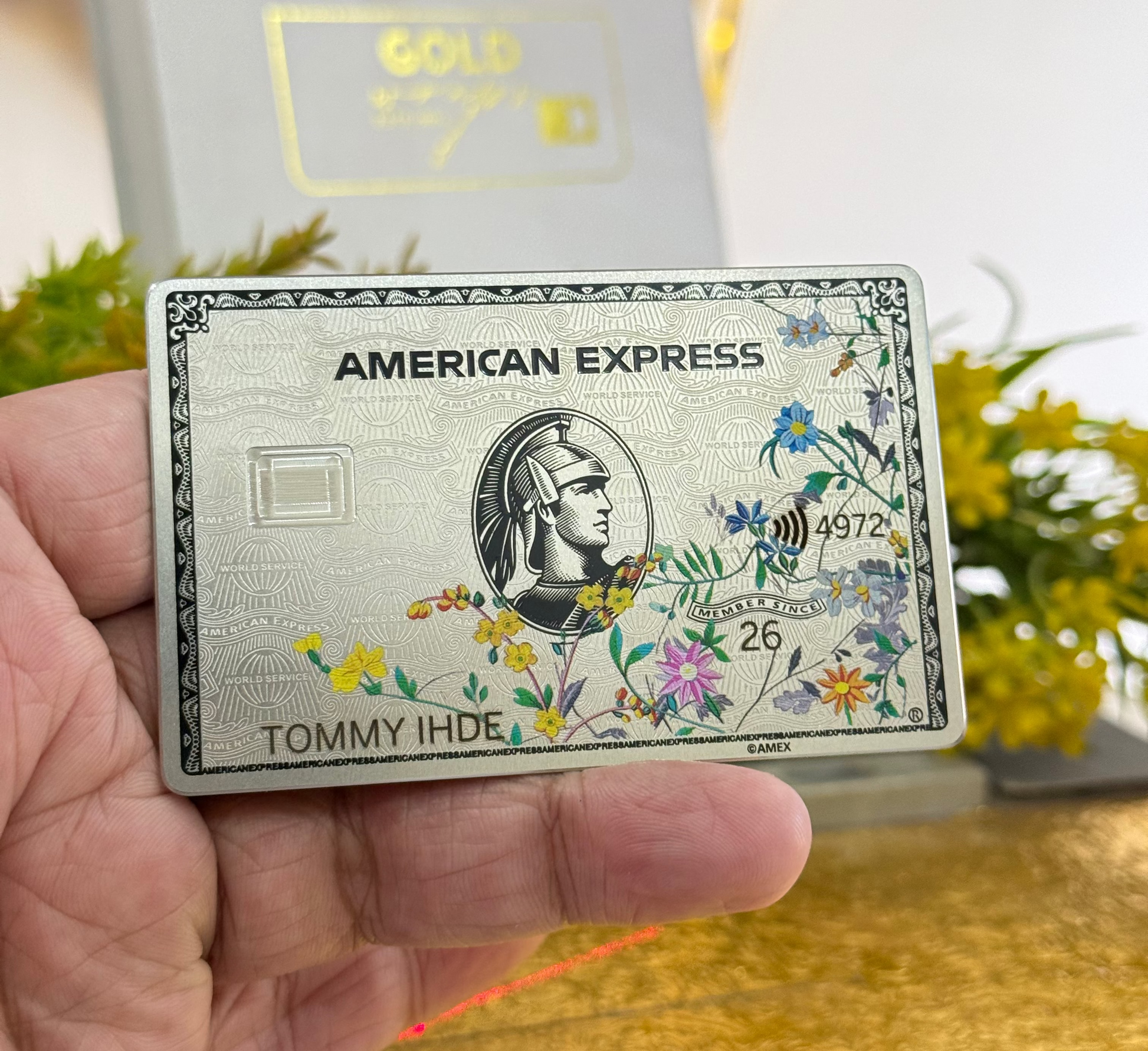 American Express Floral platinum card with leafs held by a hand with a blurred background