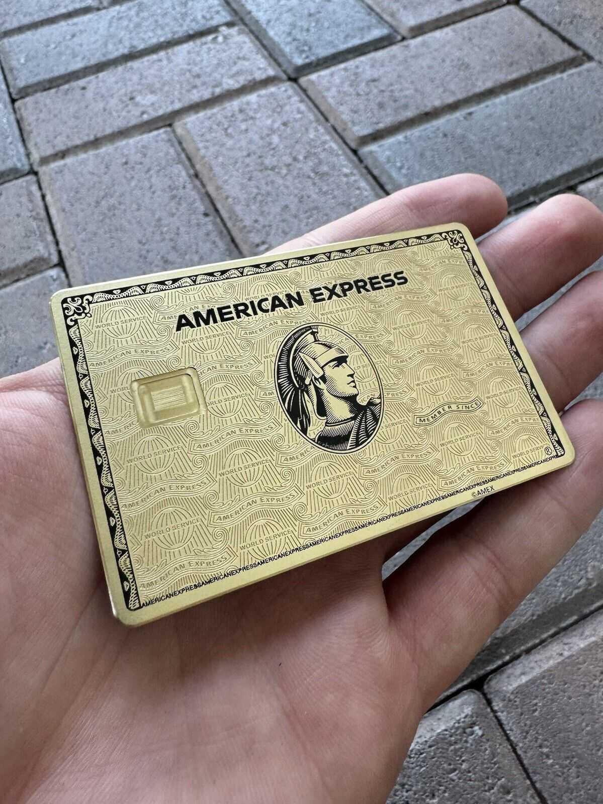 Gold American Express metal card held in hand on a stone pavement background