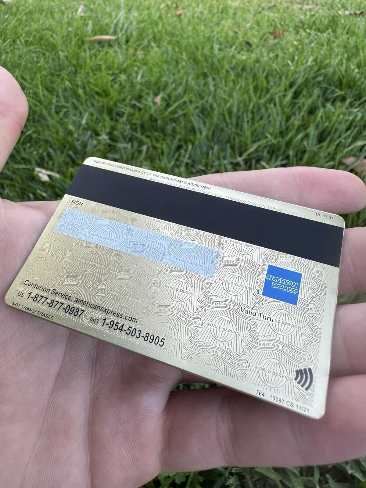 Gold American Express metal card with embossed design held in hand outdoors on grass