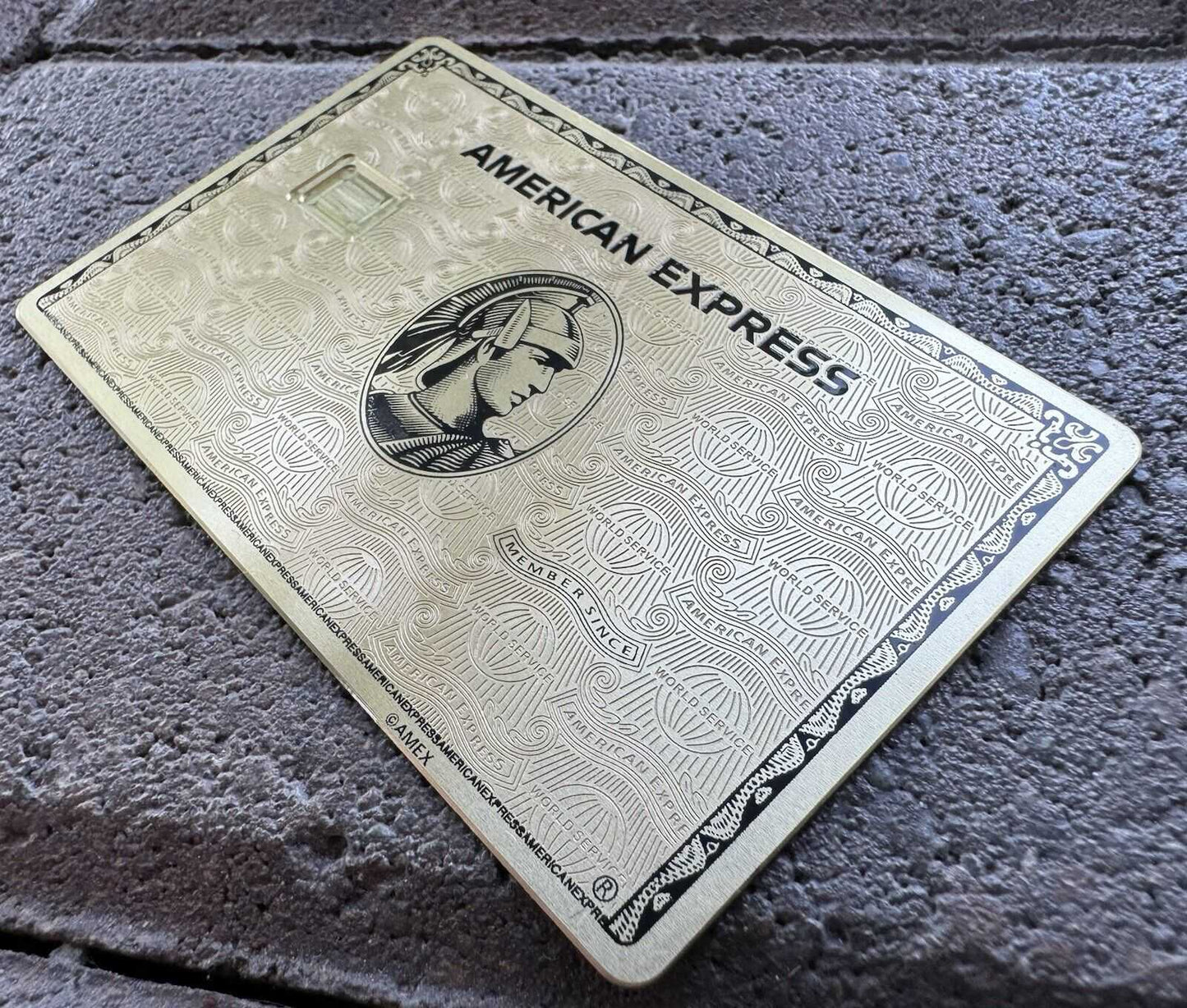 Gold American Express metal card with engraved details on a stone surface