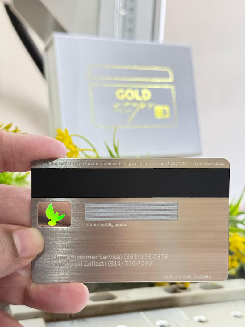 Hand holding a metal card with a magnetic stripe and holographic bird on a reflective background