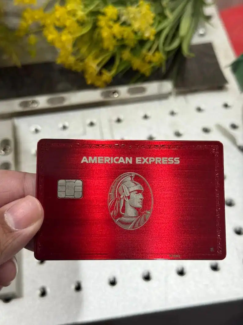 Red metal American Express card held in hand, with flowers in background