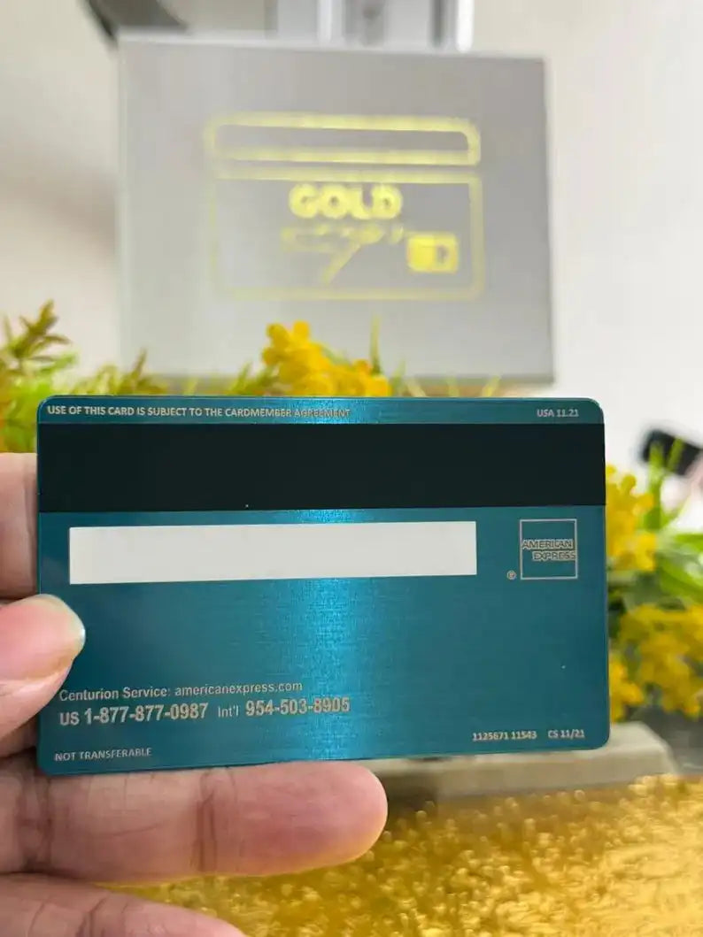 Hand holding a metal American Express card with engraved details, flowers in background.