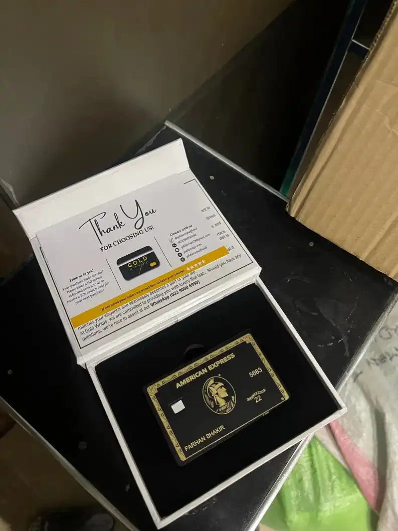 Black and gold metal card in American Express style displayed in an open gift box