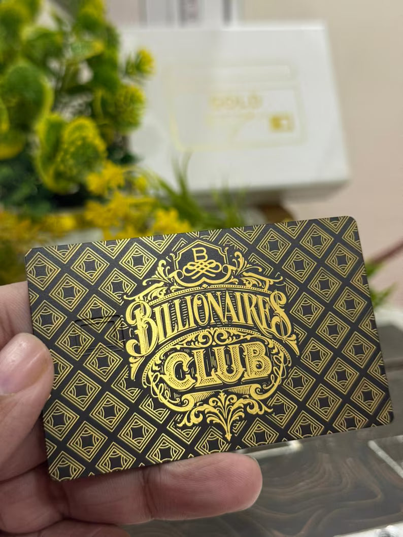 Hand holding black and gold Billionaires Club metal card with ornate geometric pattern