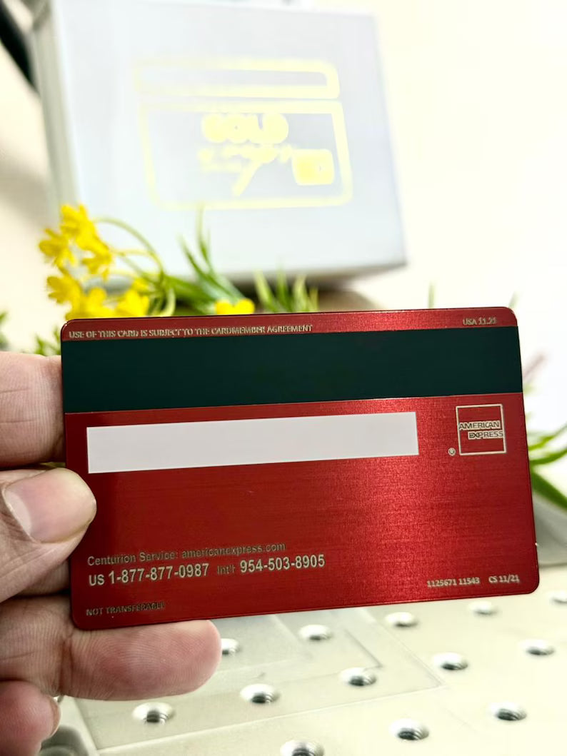 Red metal American Express card held in hand, with yellow flowers and box in background