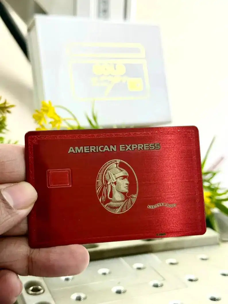 Hand holding a red metal American Express card with engraved details, card machine in background
