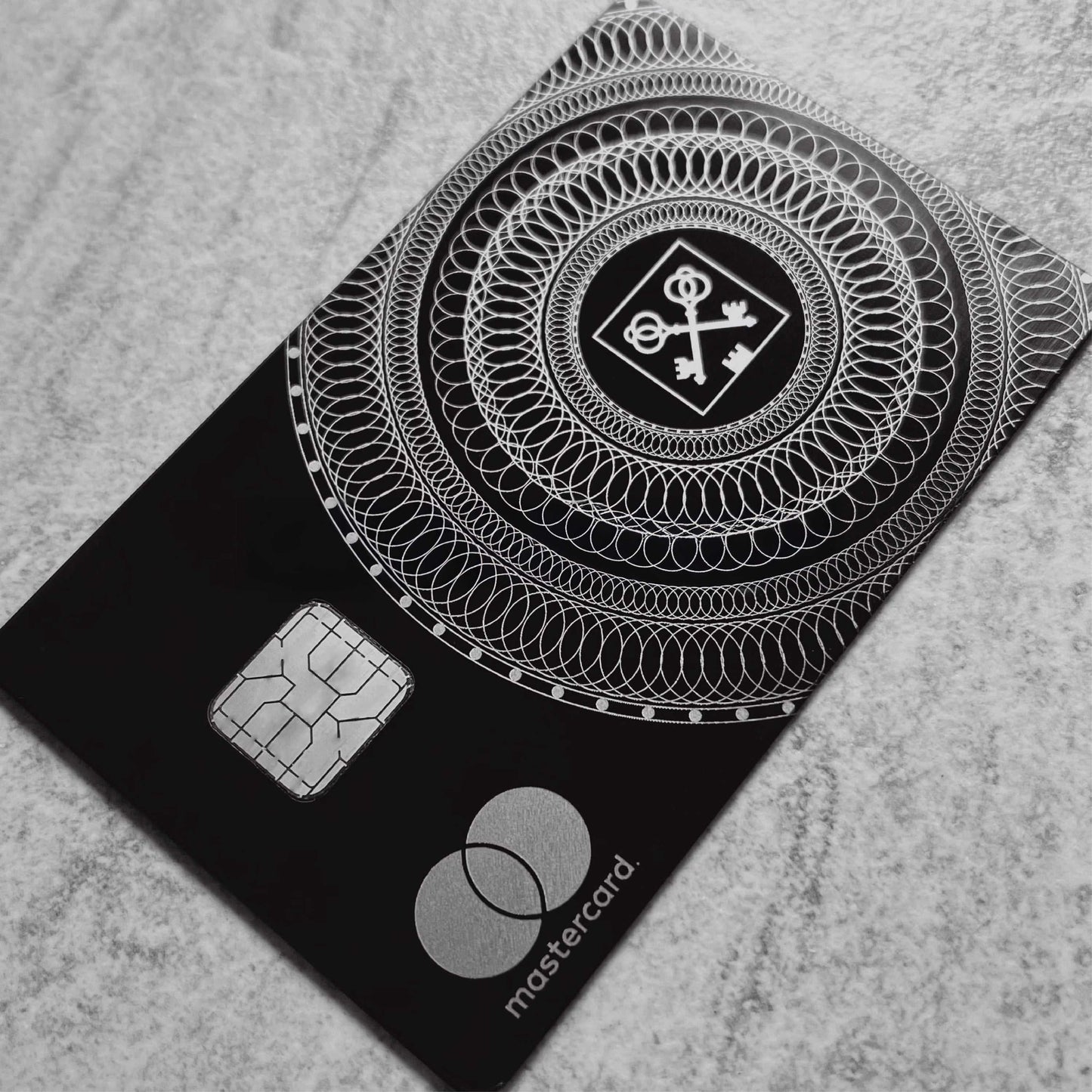 Black metal Mastercard with silver chip and intricate key pattern, luxury credit card