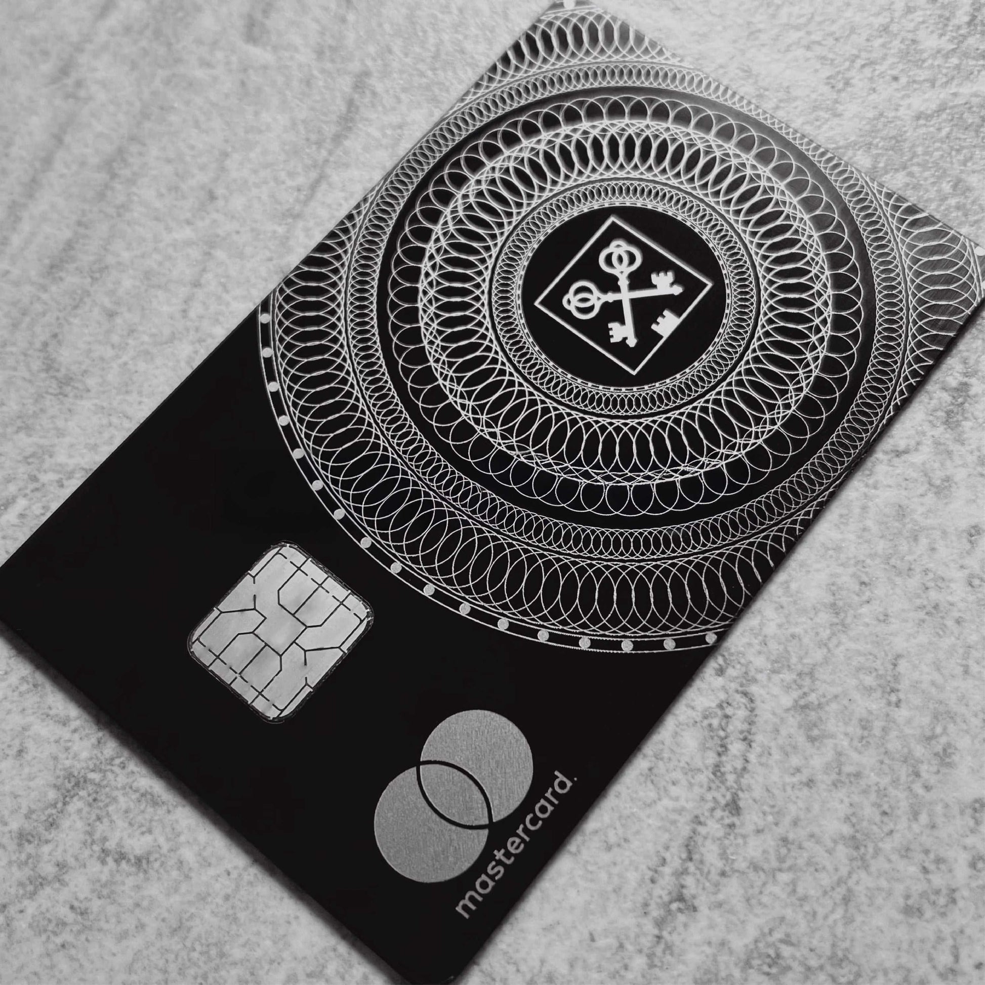 Black metal Mastercard with silver chip and intricate key pattern, luxury credit card