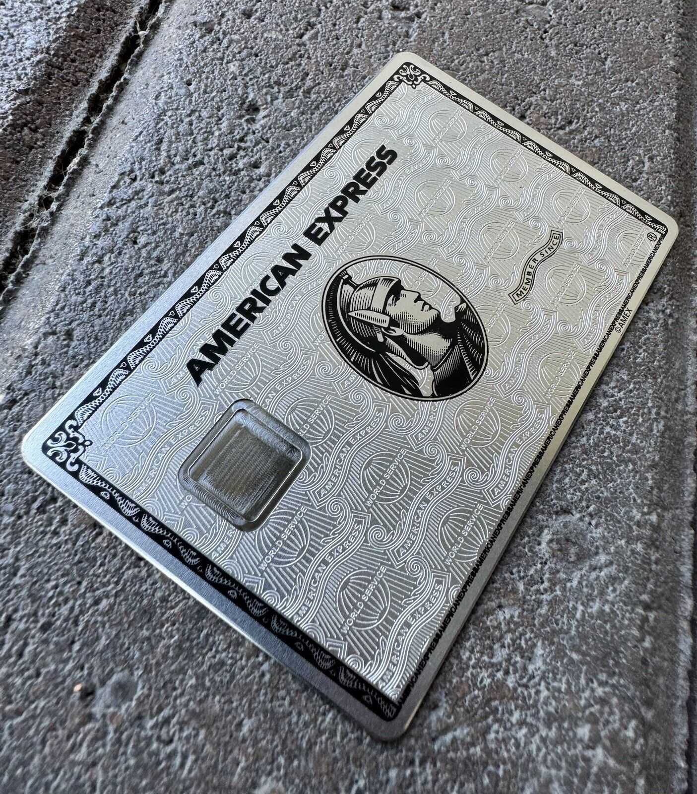 Metal American Express card with engraved details on textured gray surface